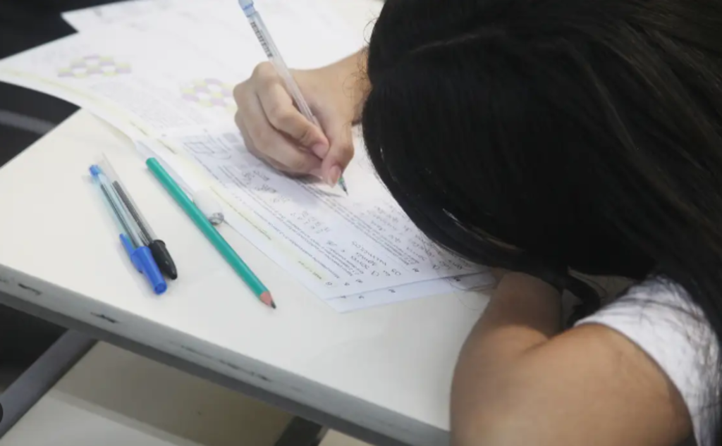 Estudante debruçada sobre uma carteira escrevendo.