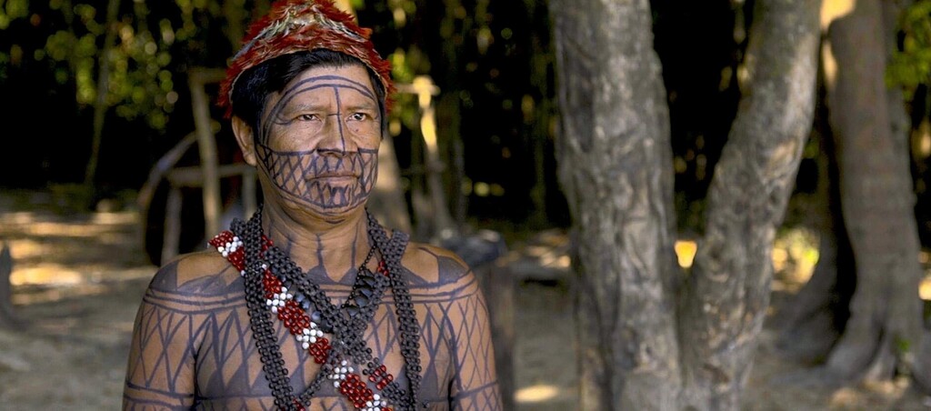 Imagem de um índio caracterizado em uma floresta.