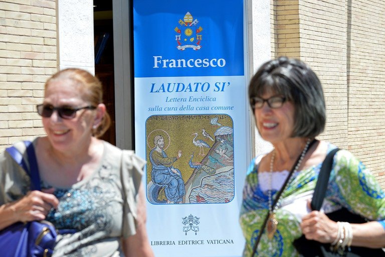Turistas no Vaticano passam por cartaz sobre a encíclica papal que tratou do clima