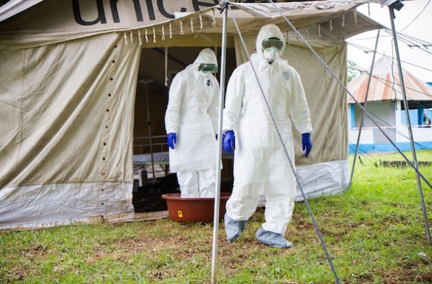 Dois trabalhadores da saúde colocam os pés em um recipiente de água com hipoclorito de sódio, à saída de uma tenda de campanha em isolamento, durante simulação de atendimento a pacientes com ebola no hospital de Biankouman, na Costa do Marfim. Foto: Marc-André Boisvert/IPS