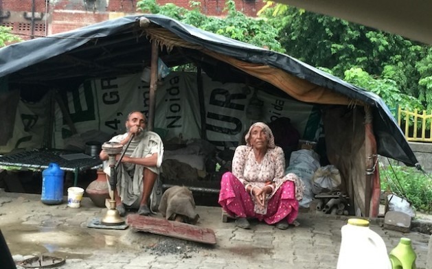 Casal de idosos sentado diante de sua “casa”, uma estrutura feita com sacos plásticos e materiais descartados. Foto: Neeta Lal/IPS