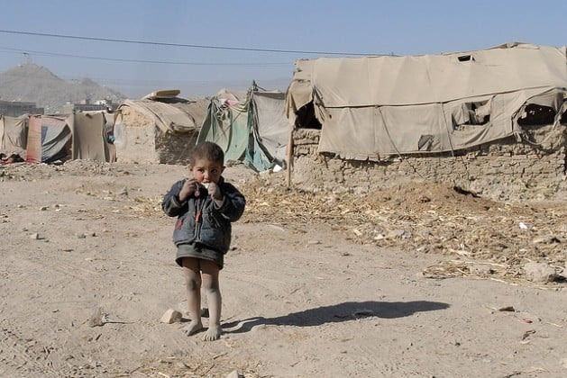 Um menino refugiado afegão come um doce em frente à barraca de campanha que sua família ocupa. Foto: DVIDSHUB/CC-BY-2.0