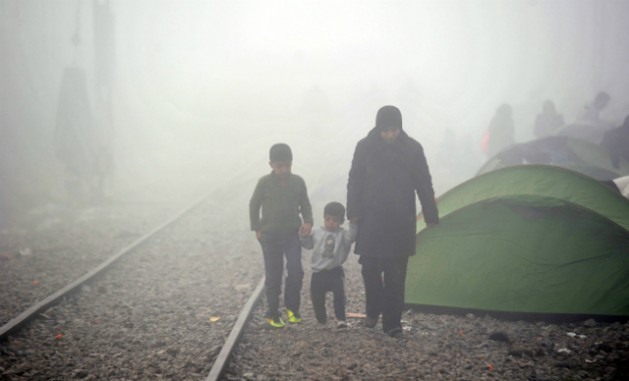 Mulher caminha com seus dois filhos ao lado dos trilhos do trem, em meio à neblina em Idomeni, na Grécia, em março de 2016. Foto: ©UNICEF/UN012794/Georgie