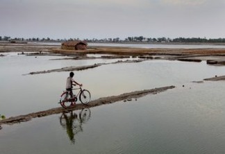Menino atravessa com sua bicicleta um longo e estreito caminho de barro em Bangladesh, um dos países mais vulneráveis à elevação do nível do mar e à frequência extrema dos fenômenos meteorológicos extremos. Foto: GMB Akash/Pnud