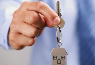Holding out house keys on a  house shaped keychain